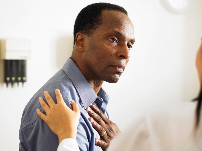 black patient in a doctor's office, with caregiver who has hand placed on his shoulder