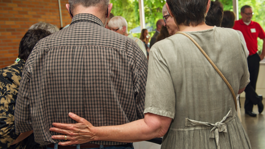 A woman places her hand on the back of a gentleman in a group setting