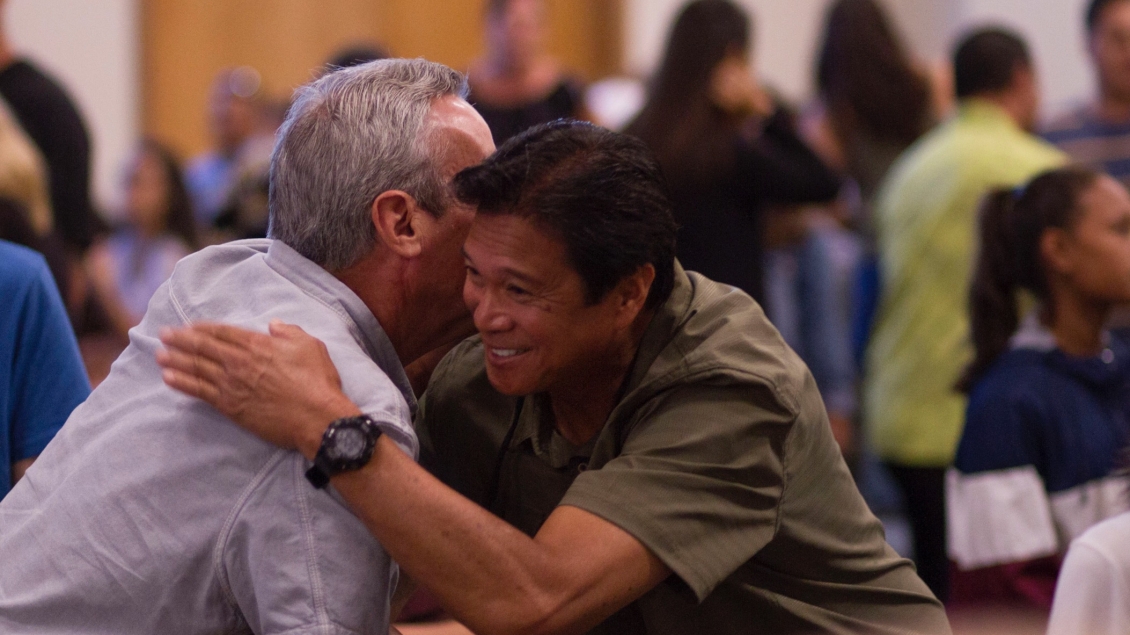 Younger man hugs older man in group setting