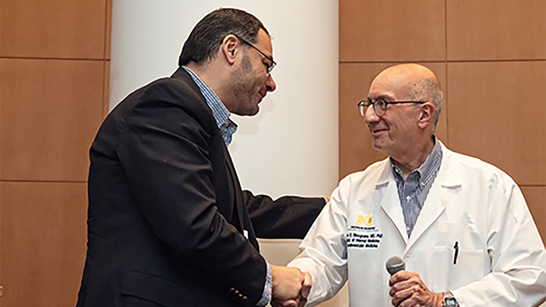 2 men smiling and shaking hands during Annual M-BoCA Symposium